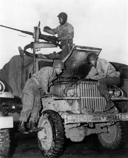 African American members of the World War II Red Ball Express repair a 2.5-ton truck while a crewman at a machine gun keeps watch for the enemy. Photo courtesy Army Transportation Museum.